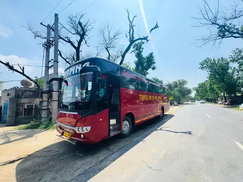 Deluxe coach, maroon livery, front three-quarter view on the road — built by Guru Kirpa Bus Body Builders, Barnala
