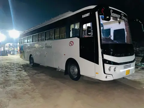 Deluxe coach, white with multicolour graphics, front three-quarter view at night — built by Guru Kirpa Bus Body Builders, Barnala